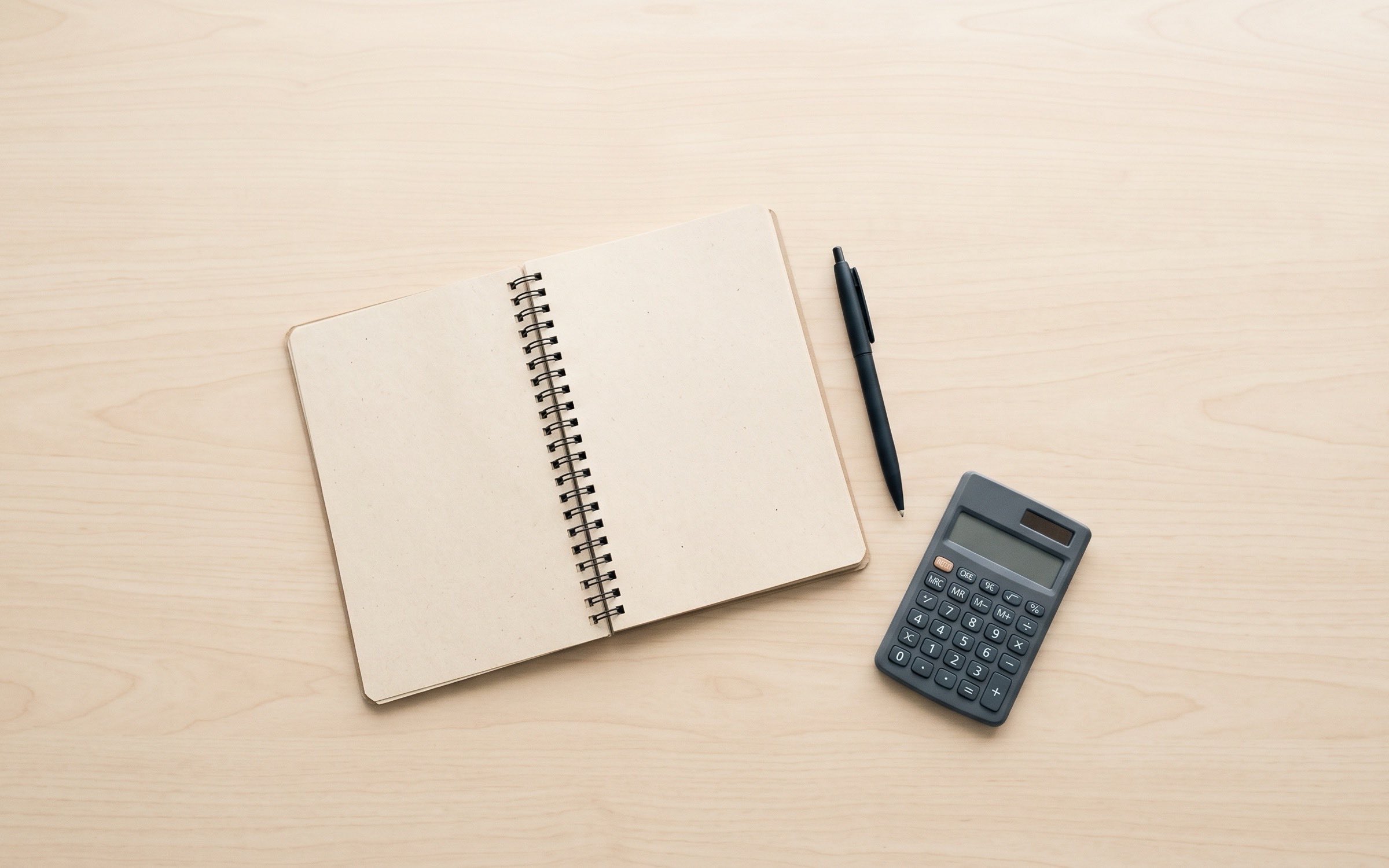 Vista cenital de una mesa de trabajo con un cuaderno abierto, un bolígrafo y una calculadora